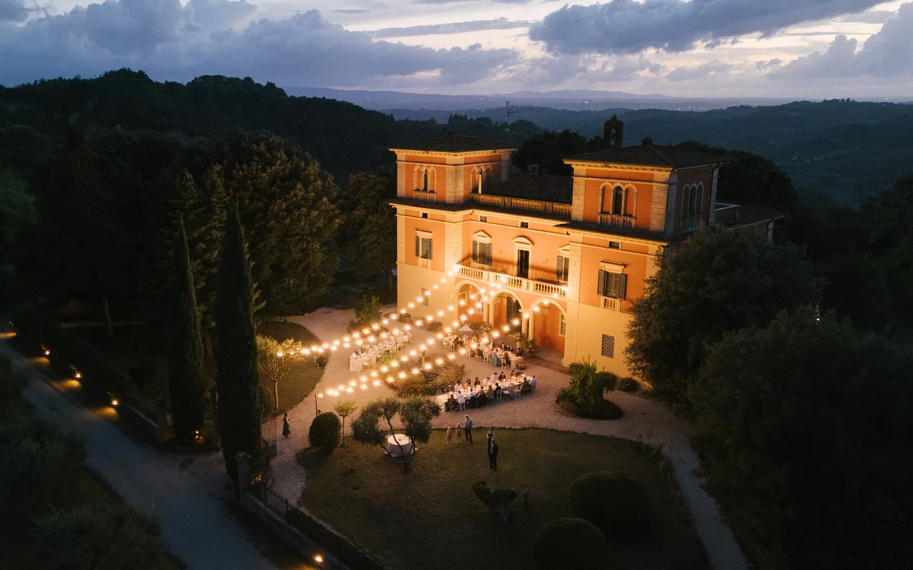 Villa Lena at dusk — dinner laid in front of the villa, lights between the trees